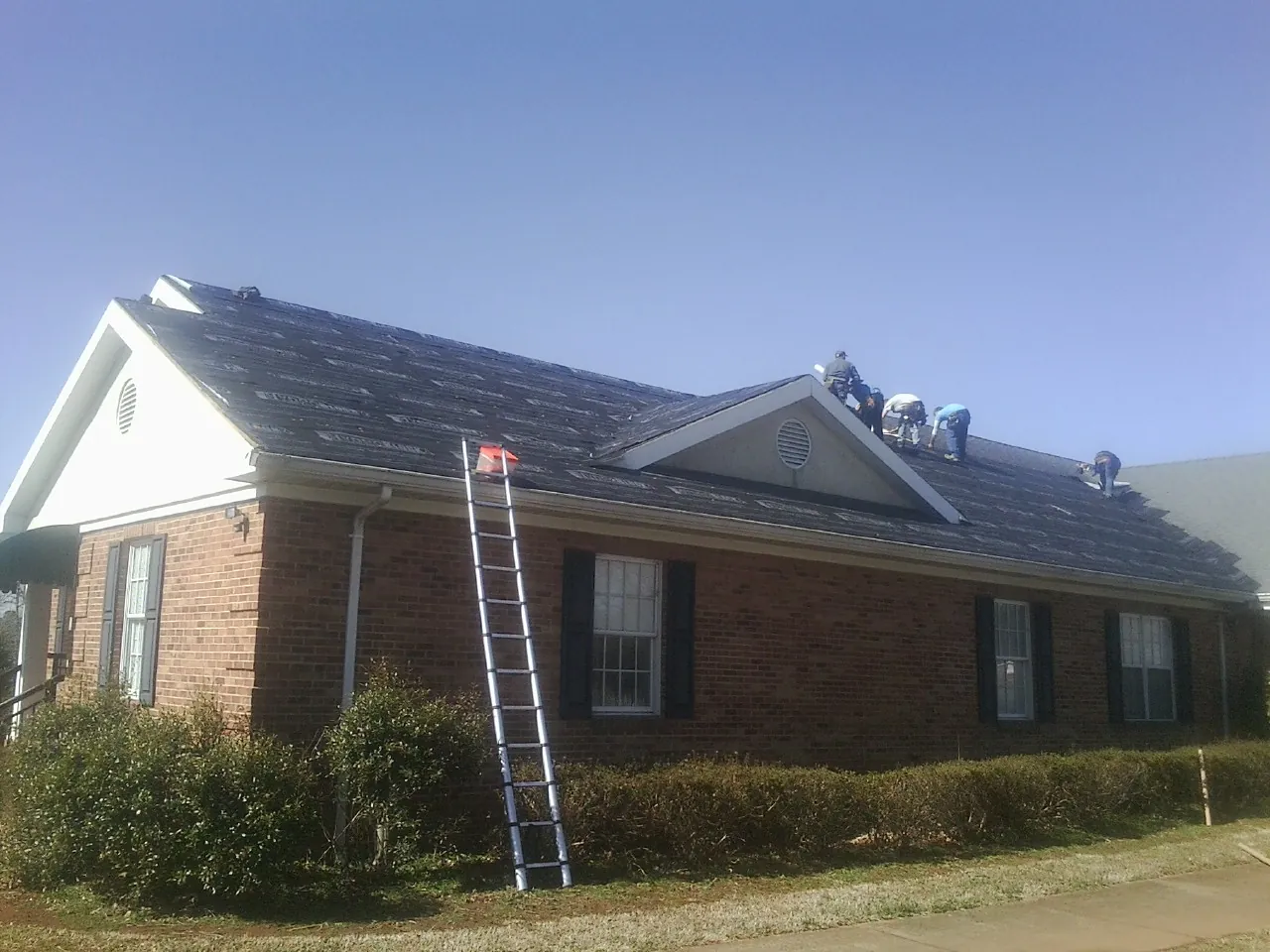 Crew tearing shingles off a brick ranch roof with a ladder set — Emergency Roof Repair work by our crew in Earleton
